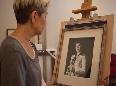 A woman with short, styled hair examines a framed black-and-white portrait of a woman holding a microphone